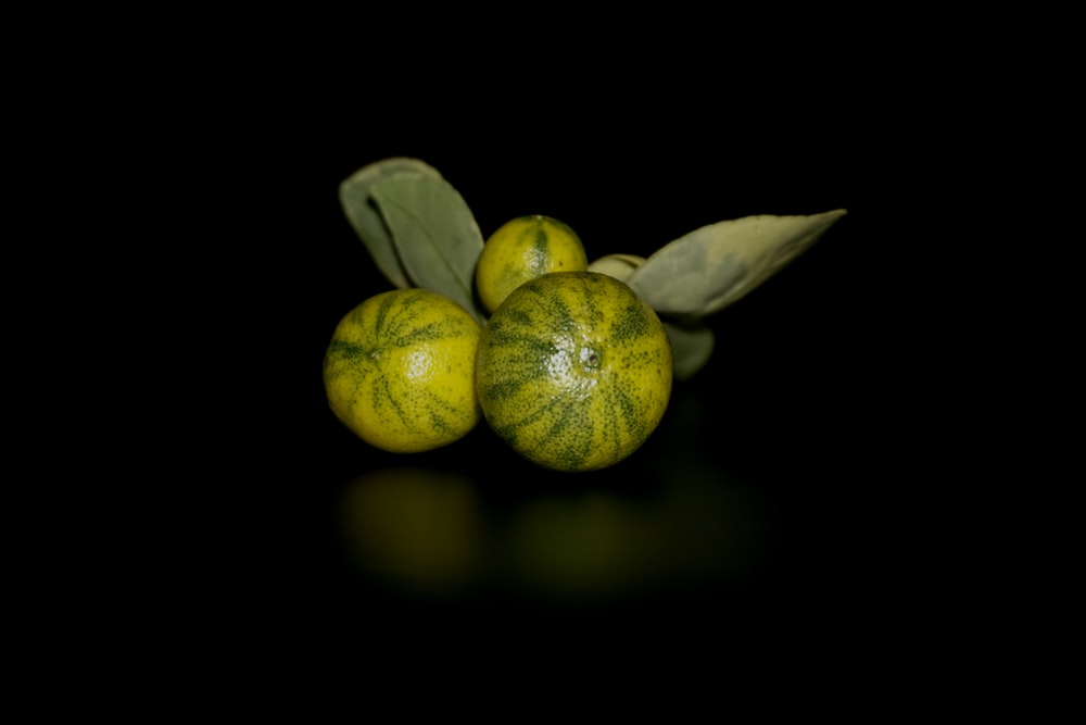 three oranges with green leaves on a black background
