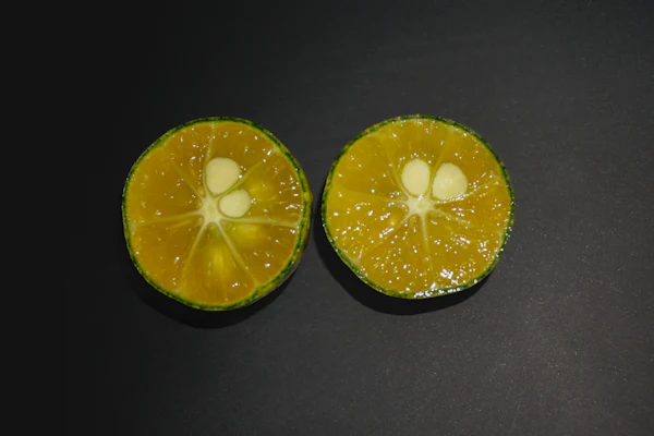 Two calamansi halves showing orange flesh, pale seeds and a thin green peel
