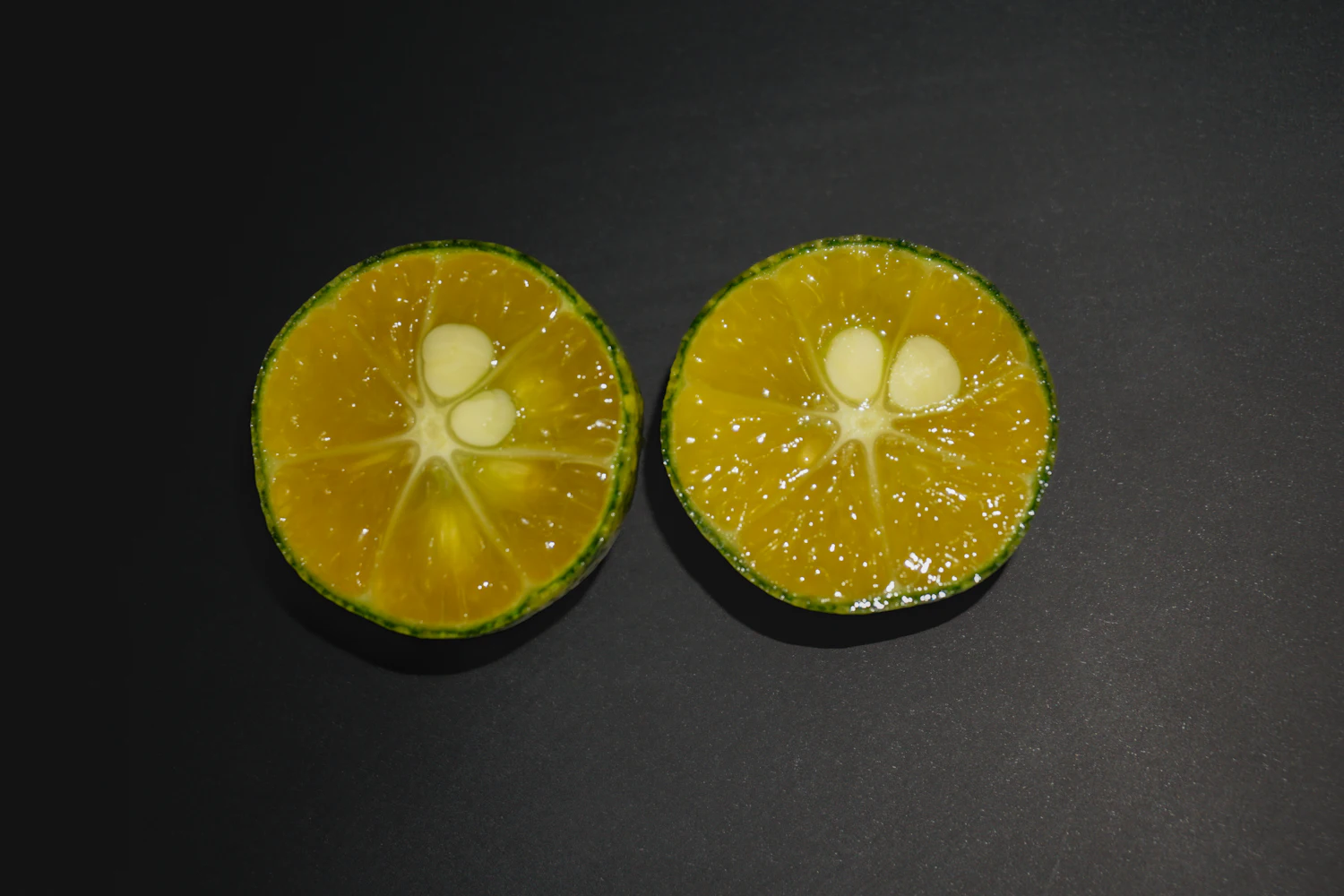 Two calamansi halves showing orange flesh, pale seeds and a thin green peel
