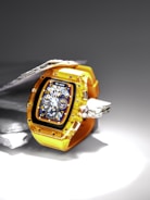 A luxury watch featuring a transparent yellow strap and casing, showcasing intricate gears and dials on a dark, detailed face. The watch is displayed against a contrasting background of metallic and stone textures, highlighting its craftsmanship.