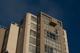 Technician inspecting a modern apartment building facade under clear blue skies.