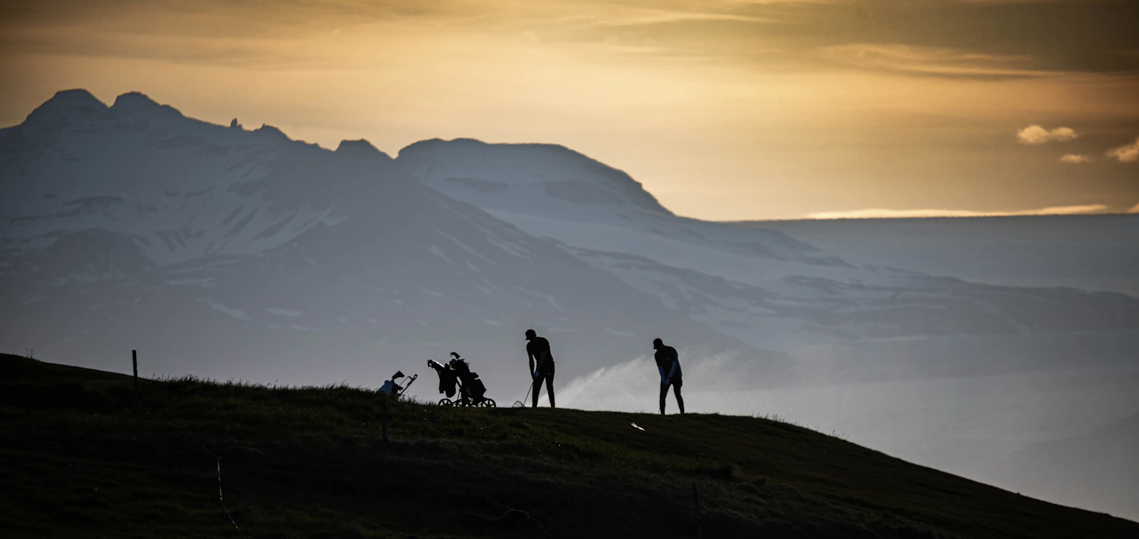 Golfers silhouetted at sunset on a hillside