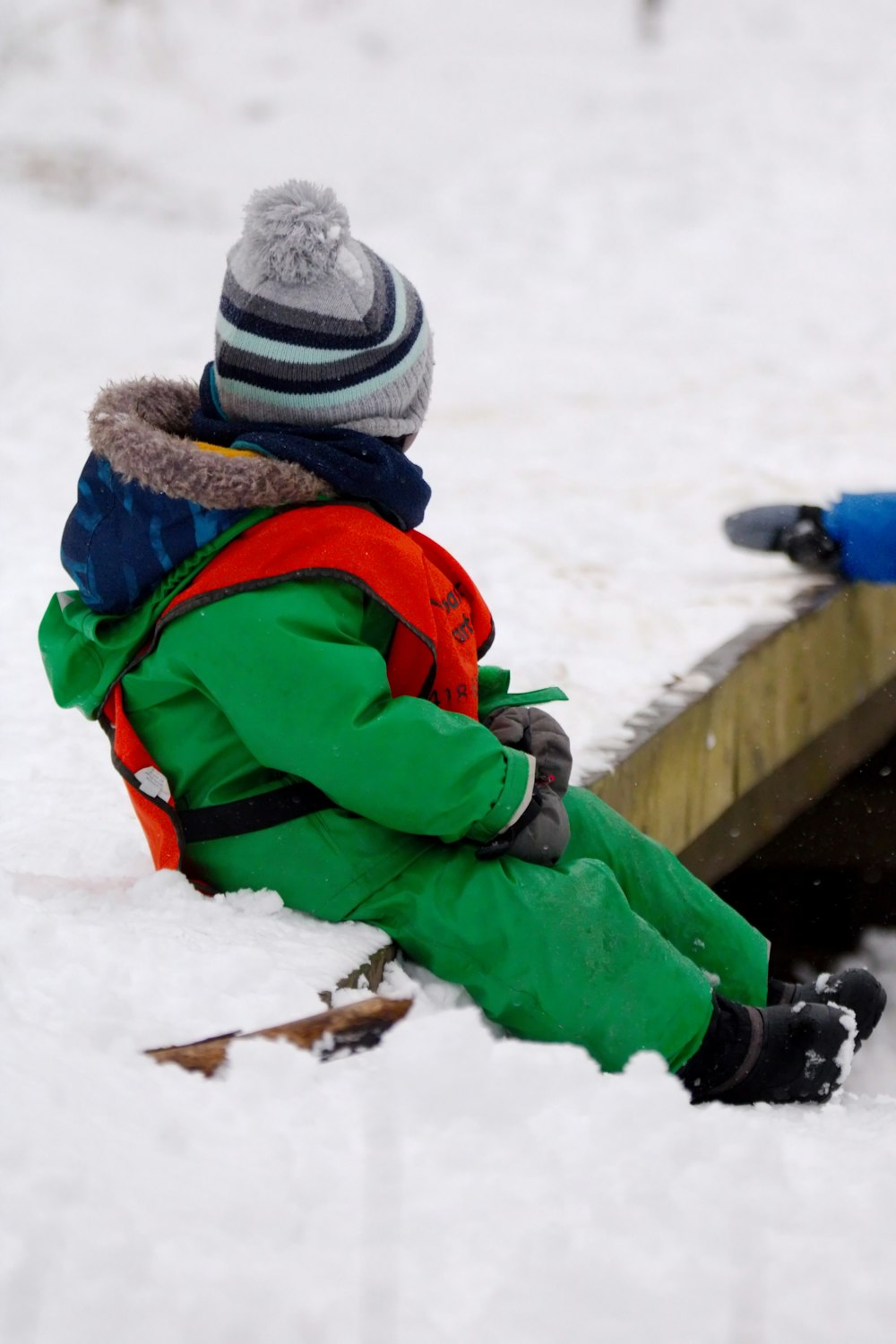a small child sitting in the snow next to a sled