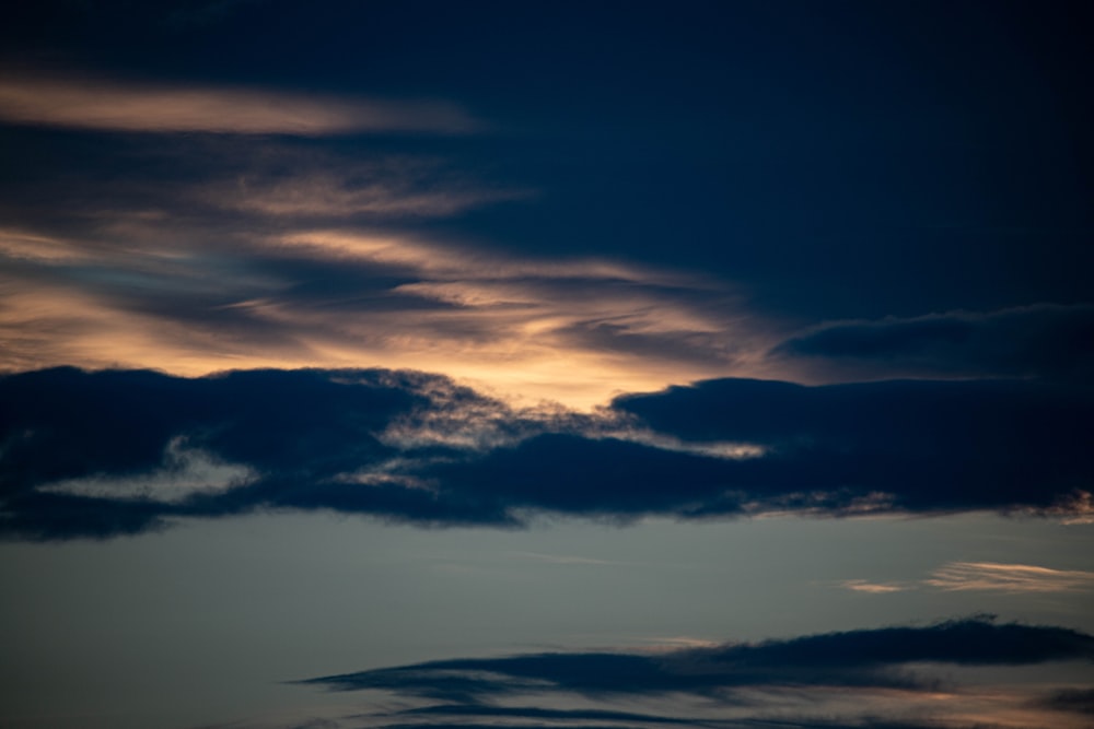 a plane flying through a cloudy sky at sunset