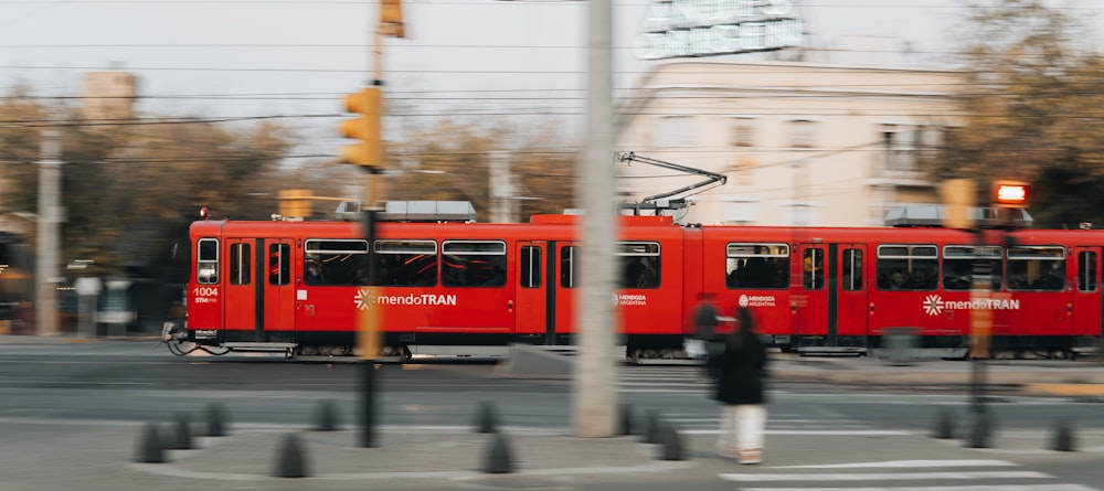 a red trolly train traveling down a street next to a traffic light