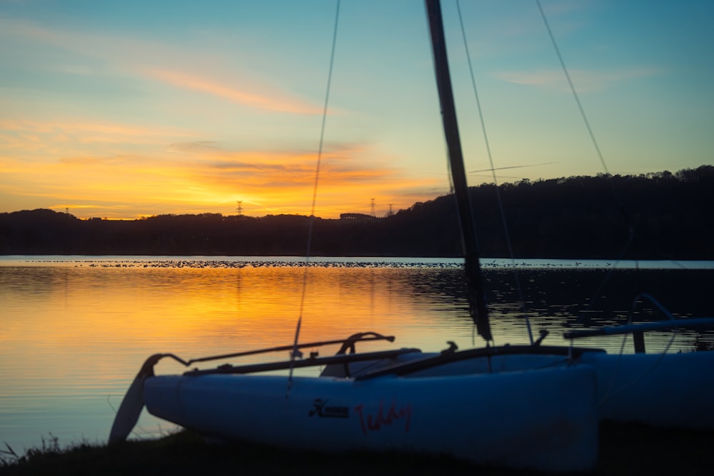 a sailboat sitting on the shore of a lake at sunset