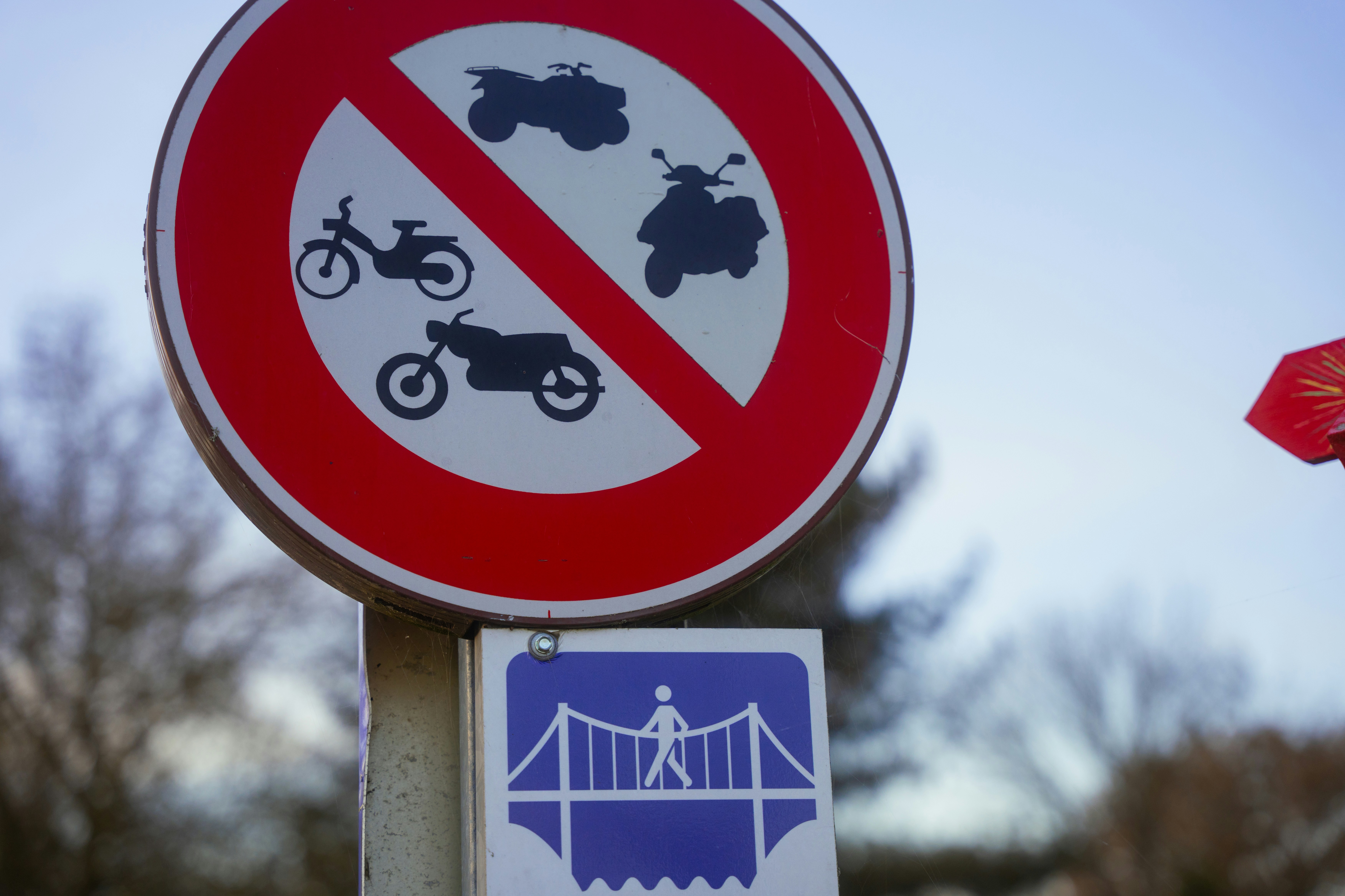 a red and white street sign with a bridge in the background