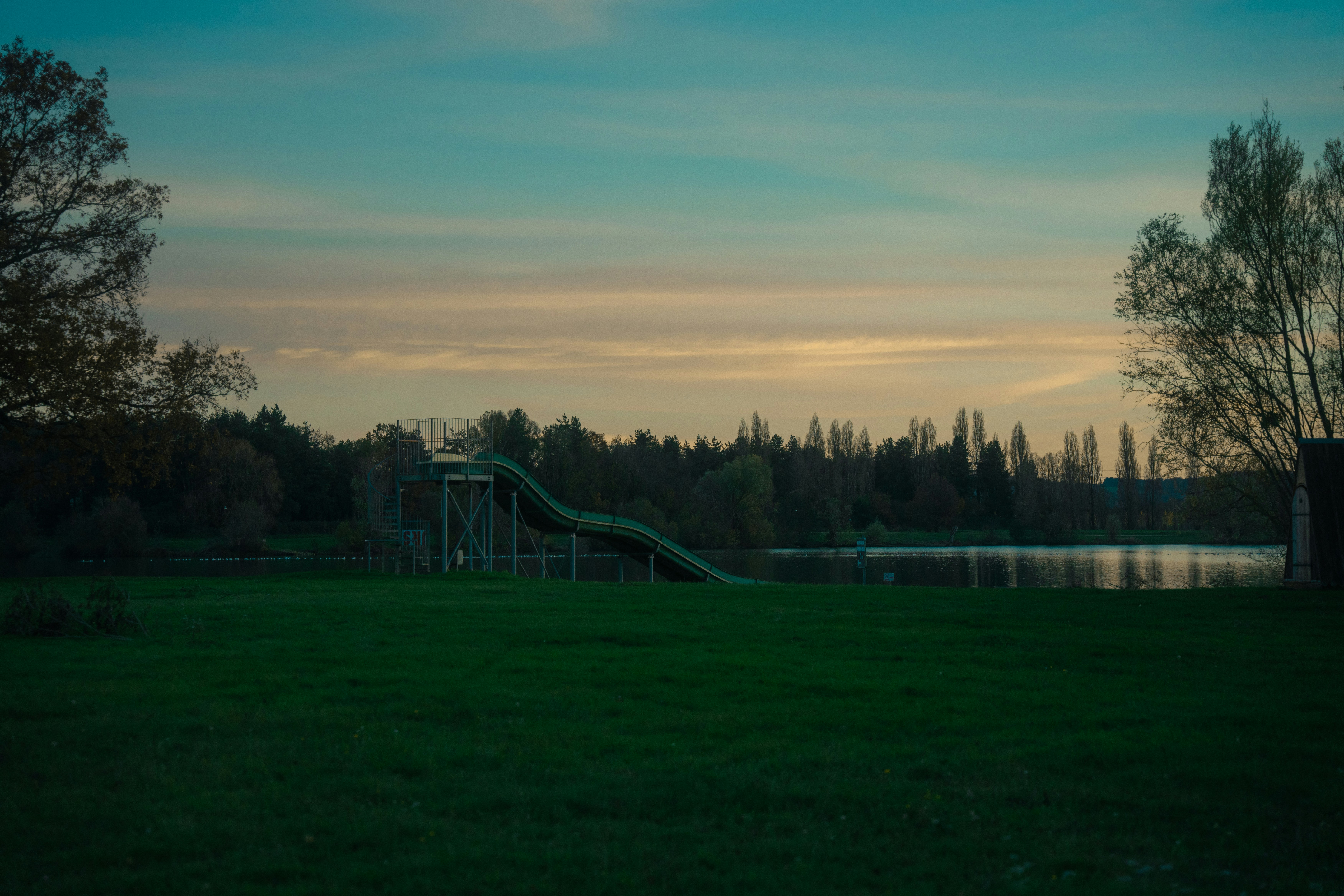 a green slide in a grassy field next to a body of water