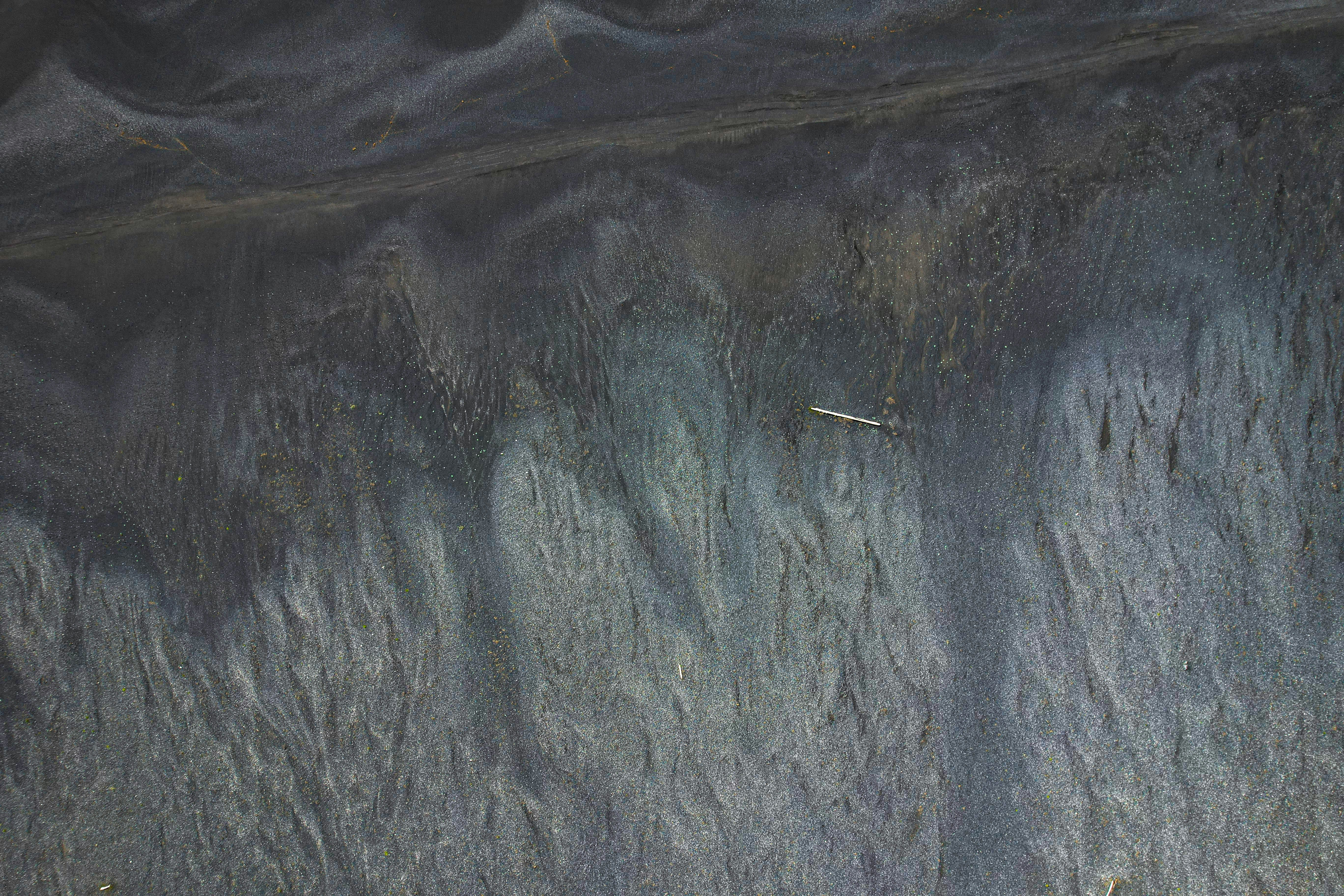 a close up of a rock wall with grass growing on it, An aerial view captures the textured landscape where a dark shoreline meets clear waters, with patterns of moss and erosion evident on the surface.