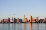 Modern Dubai skyline with towering skyscrapers reflecting in the calm water at sunset.