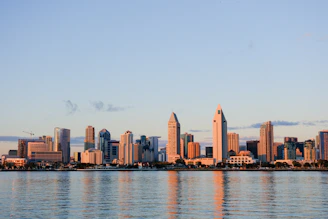 Modern Dubai skyline with towering skyscrapers reflecting in the calm water at sunset.
