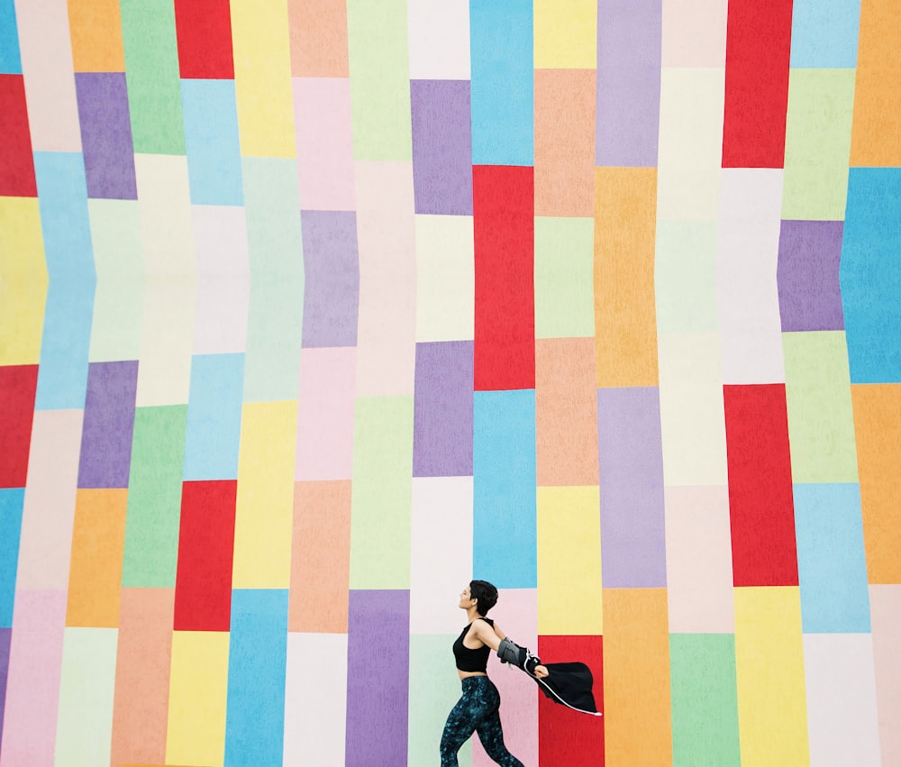 a woman walking in front of a multicolored wall