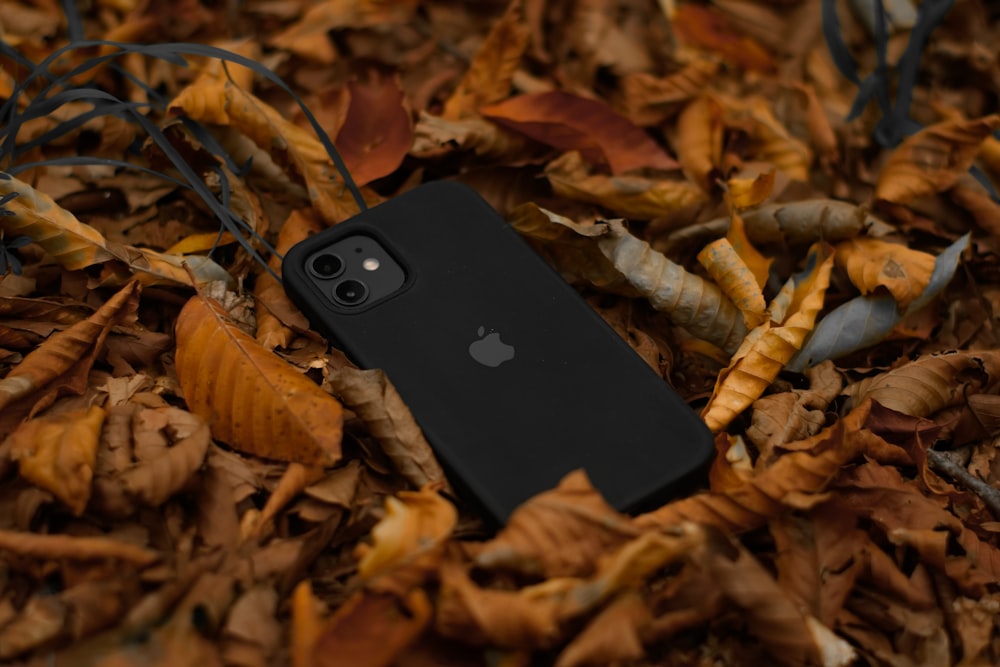 a black iphone case laying on top of a pile of leaves