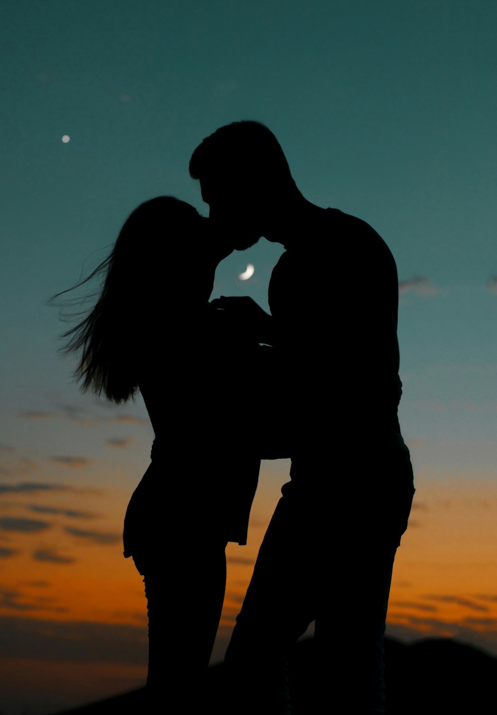 a man and a woman kissing in front of a sunset