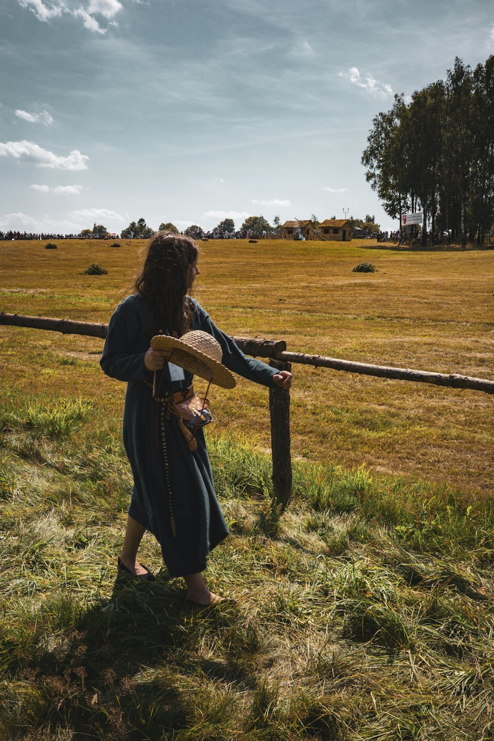 a woman in a long dress is standing by a fence