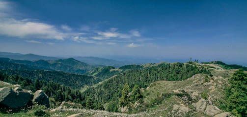 A panoramic view of Eswatini’s lush green valleys and rolling hills under a bright blue sky.
