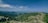 A panoramic view of lush green mountains under a clear blue sky. Dense forests cover the rolling hills, and rocky outcrops are scattered throughout the landscape.