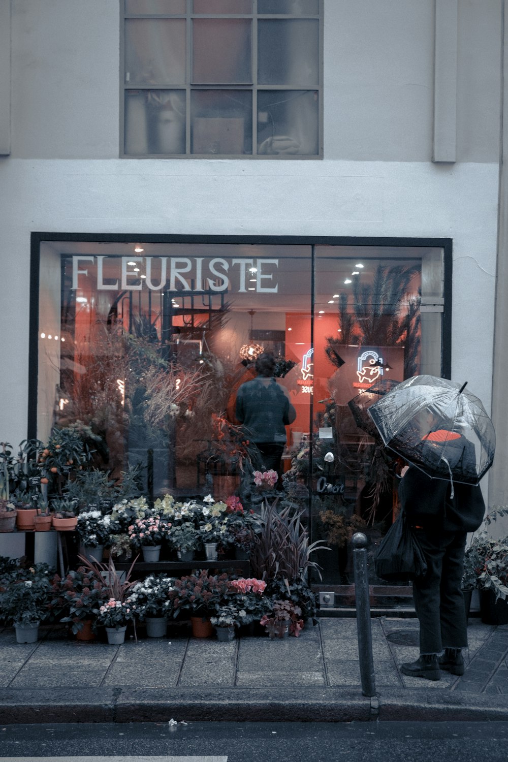 a person with an umbrella standing in front of a flower shop