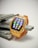 A smartwatch with a vibrant orange strap and a yellow, gem-embedded frame displaying colorful app icons on its screen. It rests on a stack of flat, gray stones against a neutral background.