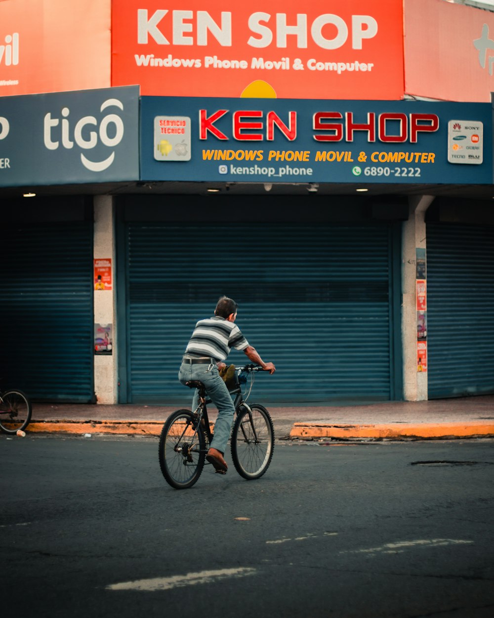 a man riding a bike down a street past a store