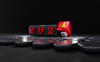 Four black cubes with the numbers 2023 are lined up, with the last cube partially turned to reveal the number 4 in red, symbolizing a transition to the year 2024. The cubes are glossy, reflecting light on a smooth, dark surface.