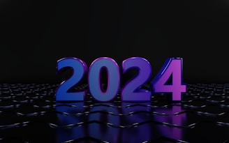 A large, glossy 3D rendering of the number 2024 stands prominently against a dark background. The numbers are illuminated in vibrant shades of blue and purple, reflecting off a sleek, tiled surface.
