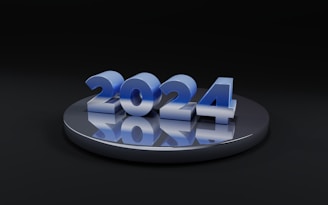 A metallic, reflective platform displays the numbers '2024' in a glossy blue finish. The numbers are prominently centered and cast reflections on the platform, creating a futuristic and sleek appearance.