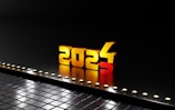 3D gold numbers forming the year 2024 stand prominently against a black reflective surface. The number 3 is falling away, indicating a transition from 2023 to 2024. Small circular lights line the edge, creating a futuristic feel.