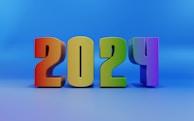 A colorful and bold representation of the year '2024' with each digit in a distinct color, set against a smooth blue gradient background. The numbers are 3D, giving them a strong and prominent appearance.
