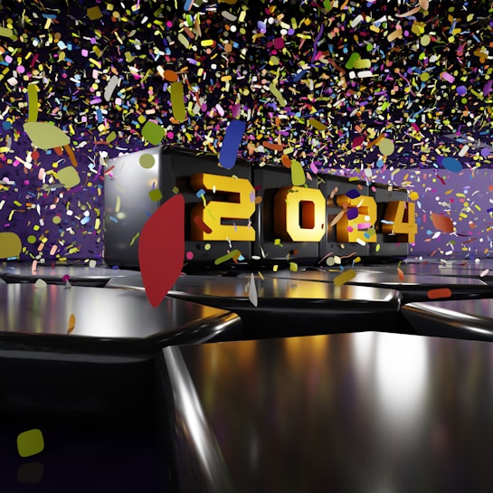 A metallic platform displays the year 2024 in bold, illuminated numbers. Colorful confetti floats through the air, creating a festive and celebratory atmosphere. The background features a mix of dark and purple hues, enhancing the vibrant contrast of the confetti.