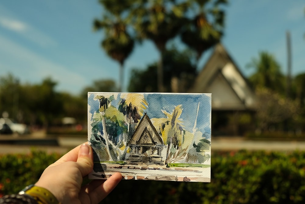 a person holding up a piece of paper with a painting on it