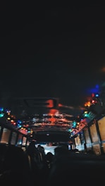 The interior of a dimly lit bus is decorated with colorful string lights along the ceiling. Passengers are seated, and their silhouettes are visible against the brightness of the lights. The atmosphere appears festive, suggesting a holiday or celebration theme.