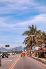 a red car driving down a street next to palm trees