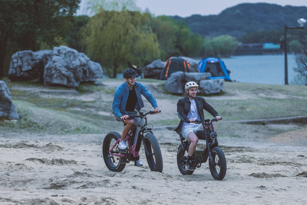 a couple of people riding bikes on top of a sandy beach