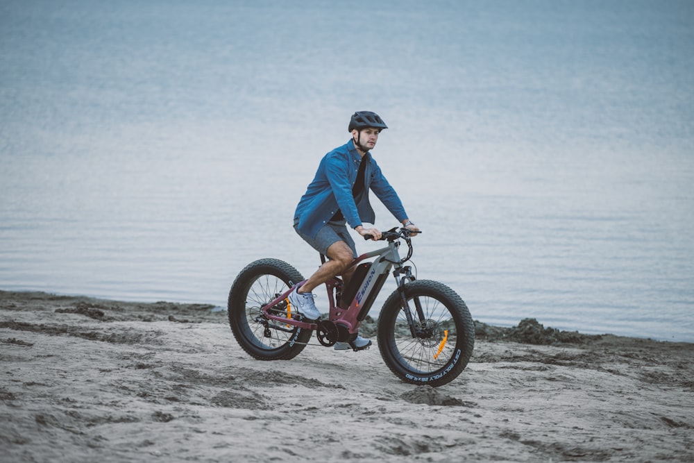 a man riding a bike on top of a sandy beach