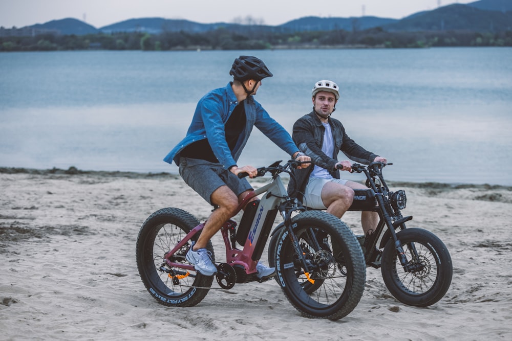a couple of people riding bikes on a beach