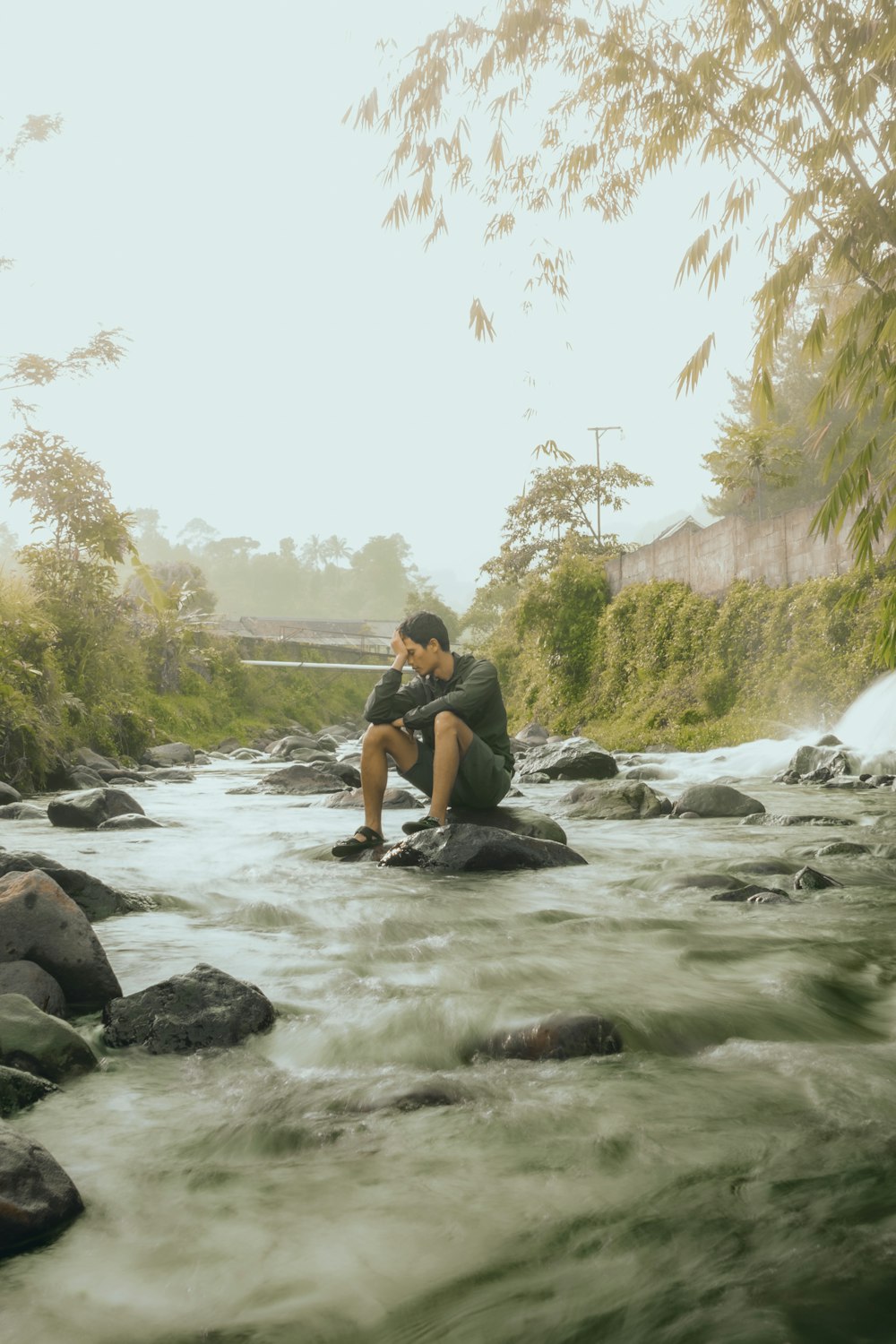 a man sitting on a rock next to a river