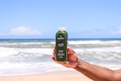 Person holding a glass of green detox juice with tropical background.