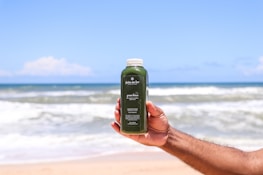 Person holding a glass of green detox juice with tropical background.
