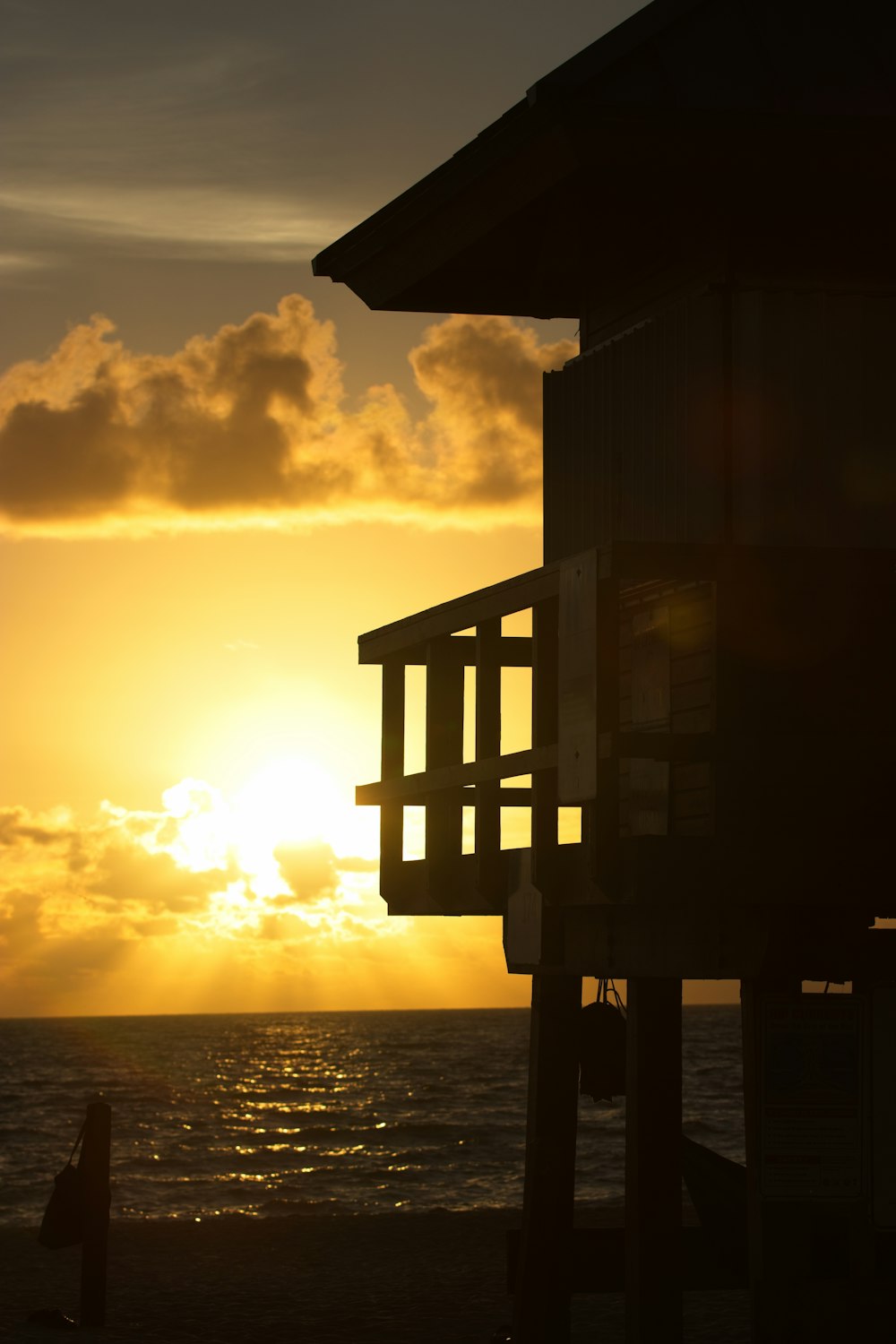 the sun is setting over the ocean with a building in the foreground