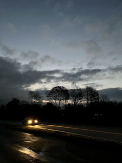 Moody cinematic frame of a car’s headlights cutting through early morning fog on an empty road.