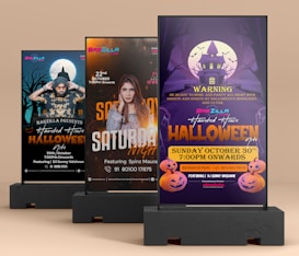 The image shows three poster stands advertising events for a club called Barzilla. The first poster on the left is for a Halloween night featuring DJ Sunny Vaishnav, with a spooky backdrop and a person wearing a Halloween-themed costume. The second poster in the middle promotes a Saturday Night event featuring Spinz Maura, with a prominent picture of the artist. The third poster on the right is another advertisement for a Halloween night at Barzilla, warning guests to be ready for a night with ghosts and spirits, featuring DJ Sunny Vaishnav, and includes Halloween pumpkins and a haunted house illustration.