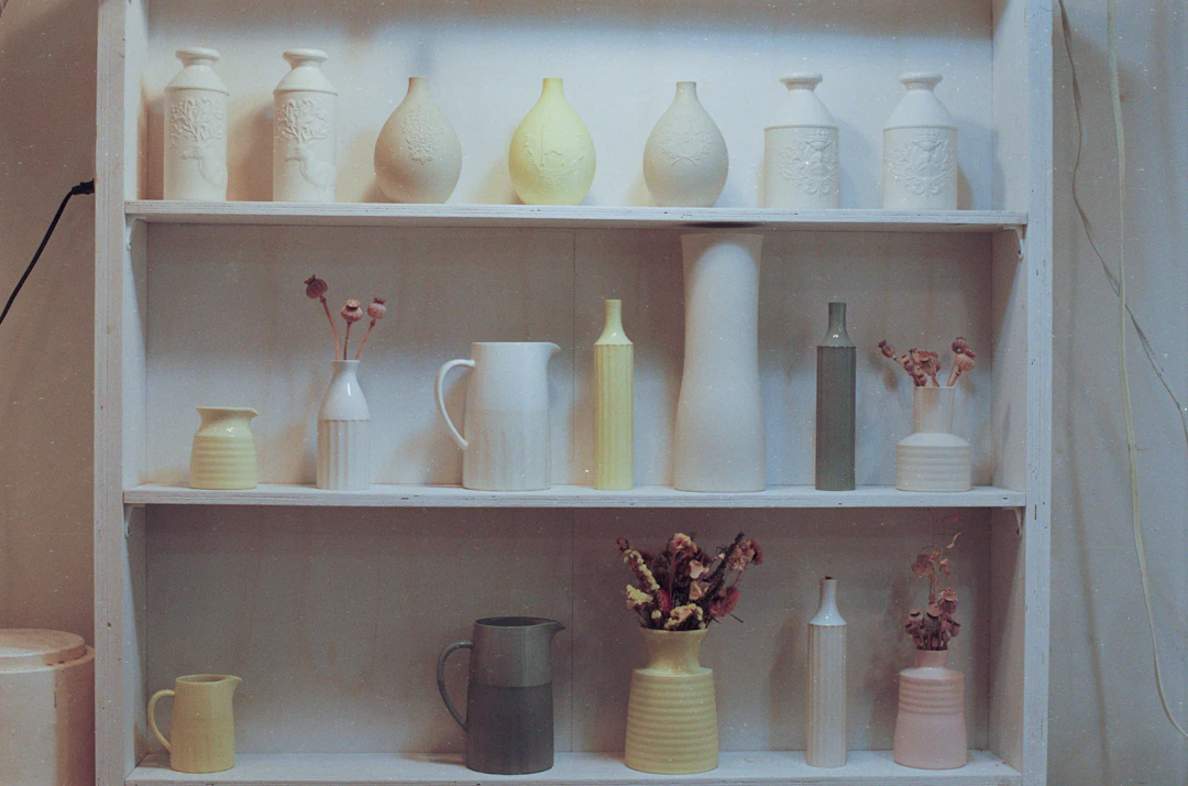 A white shelf filled with handmade vases and jugs in soft colors