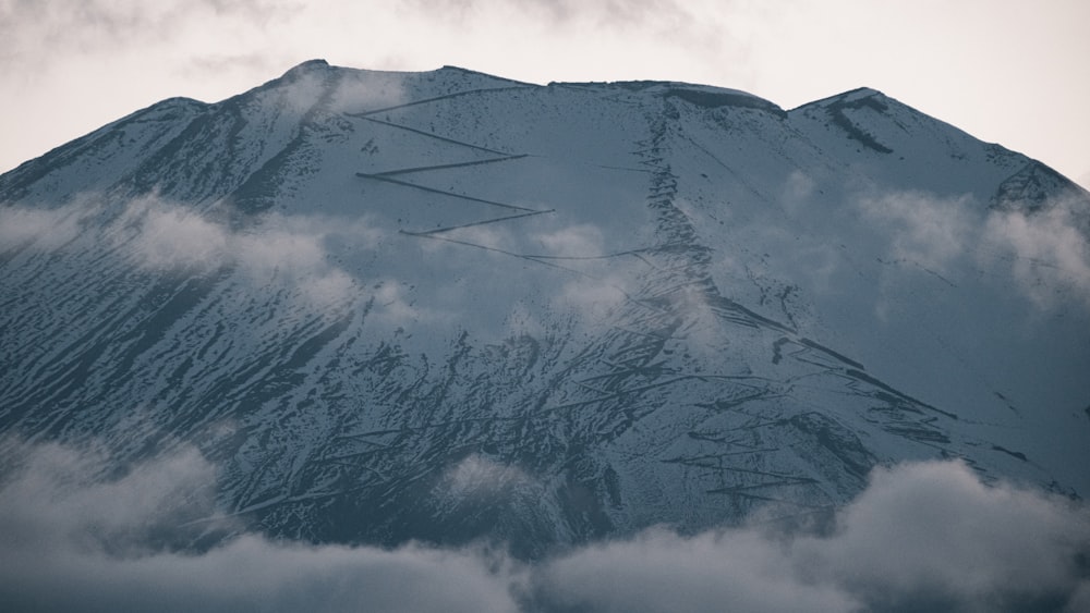 a mountain covered in snow and clouds under a cloudy sky