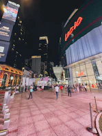 Wide shot of multiple LED screens illuminating a crowded shopping area during evening hours.