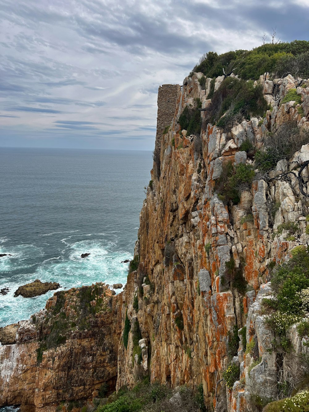 a rocky cliff overlooks the ocean on a cloudy day