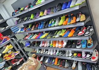 A display of various colorful athletic shoes neatly arranged on multiple shelves. The shoes come in a variety of designs and colors, including neon greens, blues, oranges, and vibrant patterns.