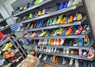 A display of various colorful athletic shoes neatly arranged on multiple shelves. The shoes come in a variety of designs and colors, including neon greens, blues, oranges, and vibrant patterns.