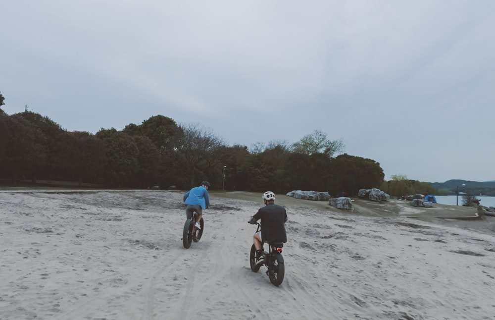 two people riding bikes on a sandy beach