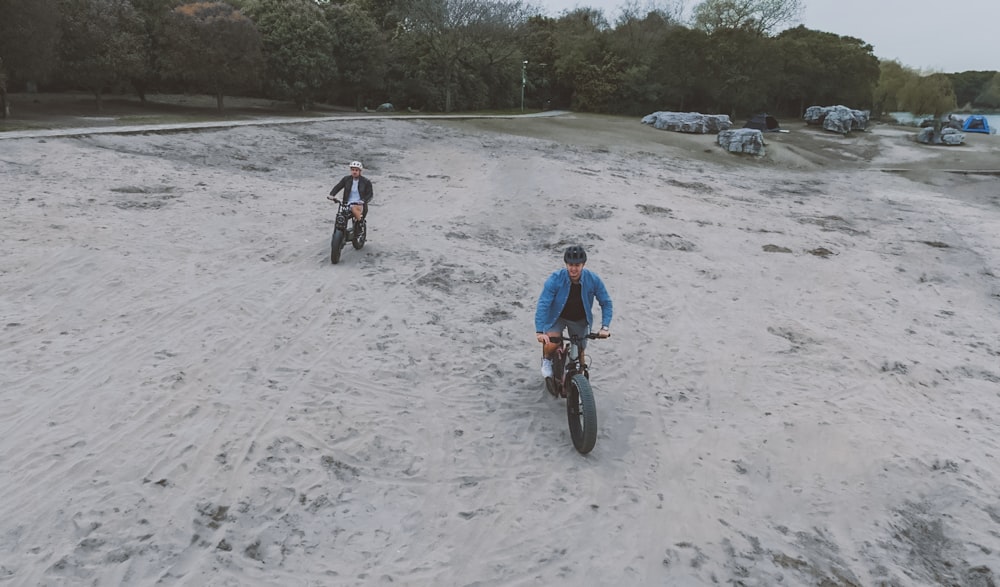 a couple of people riding bikes on top of a sandy field